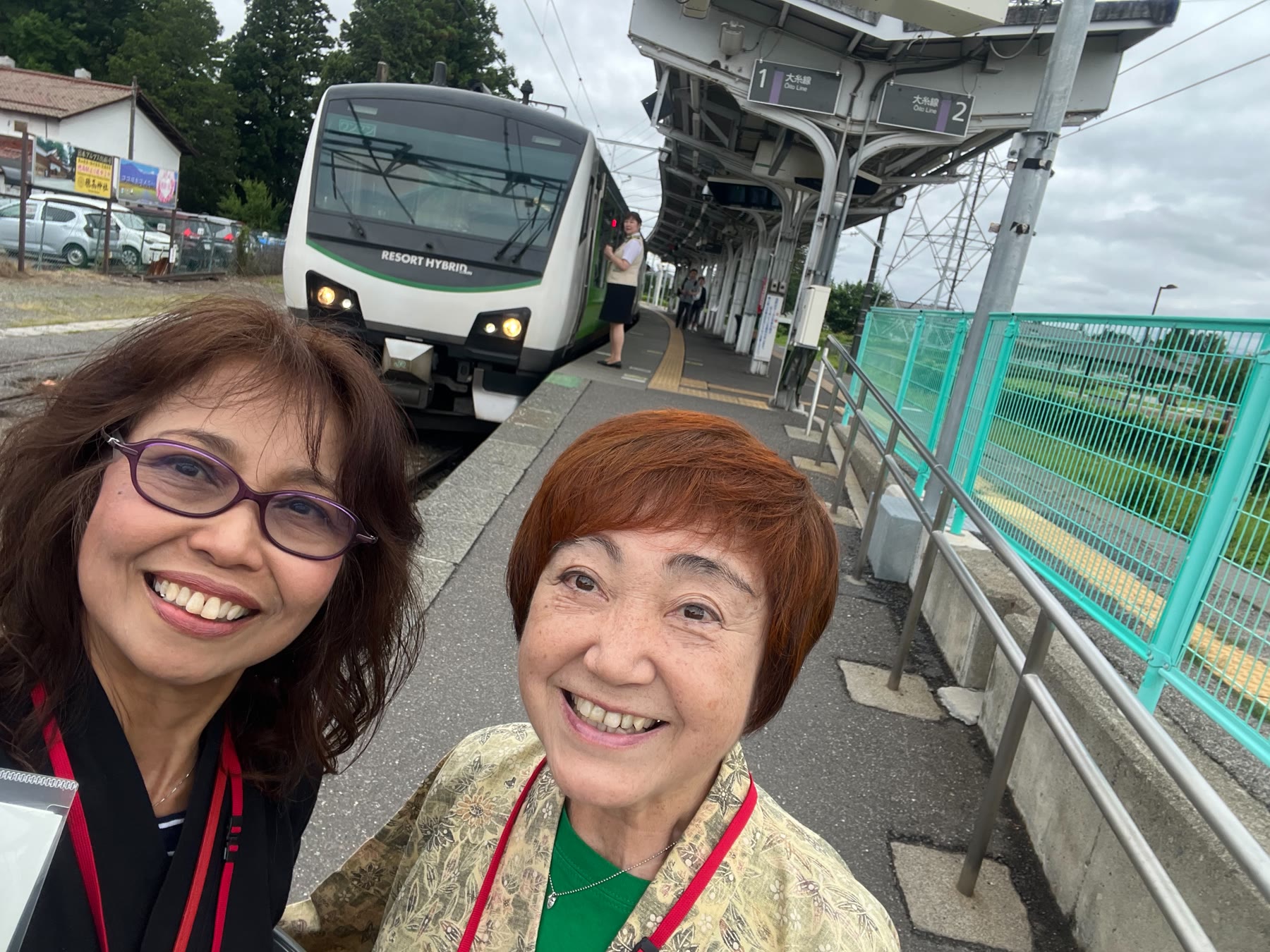 駅ホームで列車を背景に笑顔で撮影するもんぺの会会員